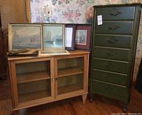 High boy chest and glass-door cabinet side by side with prints displayed atop cabinet
