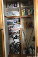 Full view of linen closet interior showing shelves with cleaning products, linens, and hanging section with brooms and bags.