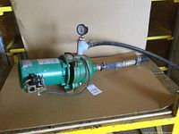 Green Myers jet pump assembly with motor, attached hoses and pressure gauge, placed on cardboard.