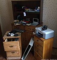 Photo showing wooden credenza, filing cabinet and three-drawer wooden chest with electronics and office items displayed on top and inside drawers.