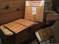 11 boxes of parquet flooring tiles in shrink wrap with some tiles removed and stacked on top. Labels read 'Do-It-Yourself Parquet Flooring Tile'.