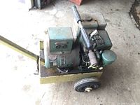 Side view showing electrical outlet box with two power outlets, green engine, muffler, and part of the yellow metal cart.