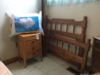 Photo showing wooden single bed headboard and footboard leaning on wall, CloudSoft pillow in package on the floor next to the bed components, and wooden nightstand with drawers next to bed parts.