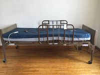 Full side view of electric hospital bed mounted on casters with metal side rails and blue mattress.