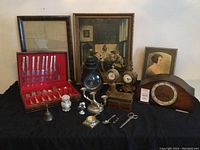 Wide view showing boxed silverware, framed prints, clocks, figurines, and various small collectibles on table