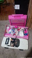 Barbie Fold N Fun House carry case open with various dolls and doll clothes inside, with Barbie and Ken dolls inside white Corvette toy car in front.