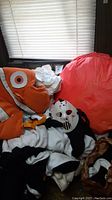 Photo showing a large orange Nemo fish costume headpiece, white costume pieces, black hooded robe, and a Jason-style hockey mask, among other costume parts piled together