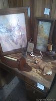 Overall view of deer statue, framed art prints, and some decorative items on wood finish desk