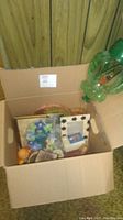 Box with assorted decor including frames, ceramic egg, plastic birdcage bottle, and other items