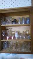 Full view of wooden shelves filled with assorted glassware including drinking glasses, mugs, and vases.