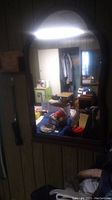 Full view of rectangular wood framed mirror hanging against a paneled wall showing a cluttered room reflection.