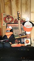 Wide view of Orioles memorabilia including banner, team photo, plush puppet, two baseball caps, Brady Anderson poster in tube, glass mug, and mini bat.