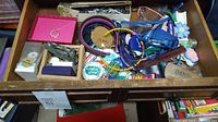 Drawer containing assorted watches, keychains, badges, and other accessories in various containers and boxes.