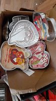 Overview of cake pans in box featuring several character-shaped pans and others with colorful paper decor inserts