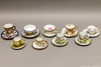 Photo showing all 9 pieces of antique Asian hand painted porcelain demitasse teacups and saucers arranged in a row.