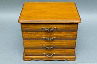 Closed wooden jewelry box with three drawers and metal handles