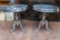 Front view of pair of aluminum side tables showing round tops and tripod pedestal bases