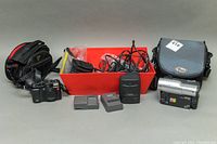 Full lot overview showing Canon G10 digital camera, Canon Vistura Mini DV camcorder, accessories including battery charger, batteries, cables, remote, and two camera bags.