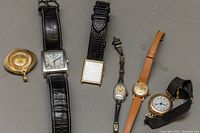 Six vintage watches laid out in a single row showing both pendant and wristwatches to illustrate the variety and condition.