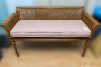 Front view of vintage wooden bench with cane meshing and pink cushion on wooden floor.