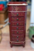 Front view of red wooden floor-standing jewelry box with multiple small drawers and hand-painted floral details.