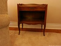 Front view of one wooden end table showing drawer with metal handle, open cubby, curved legs