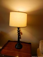 One lamp lit showing dark wood turned base and beige corsetted shade with tassels