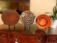 Three decorative glass platters on black metal stands displayed on furniture surface
