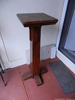 Tall wooden plant stand with cross-shaped leg pedestal base and square top, dark stained wood finish, visible minor surface wear.