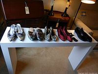 Five pairs of assorted women's shoes placed on a white table, showing variety of styles and colors in good condition.