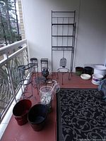 Photo showing overall assortment of garden décor on a balcony including the tall metal plant rack, several smaller metal stands, ceramic pots, and metal pails.