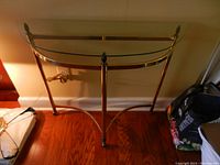 Front view of brass demi-lune table with glass top against wall on wood floor.