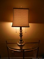 Brass table lamp with white square corset shade illuminated, showing lamp details and pull chains.