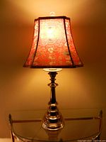 Brass table lamp with red floral corset-shaped shade illuminated, showing lamp and shade in full view.