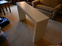 Overall angled view of white console table showing narrow rectangular minimalist design with solid sides and backless structure.