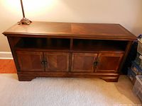 Front view of wooden entertainment console showing four paneled doors with metal knobs, and two open shelves above the doors