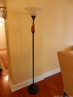Full image of the tall black floor lamp against a wall on hardwood flooring.