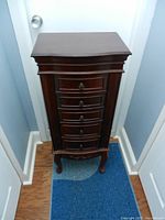 Front view showing five stacked drawers with round brass knobs, dark polished wooden finish, narrow profile with carved decorative details at base and legs.