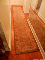 Long shot of tan and red tapestry runner rug rolled out on wood floor in hallway showing full length and tan border.
