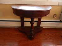Front view of the wooden demi-lune table showing the smooth half-moon top, central pedestal leg, and overall shape.