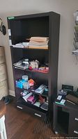 Front view of the dark wood bookshelf filled with various personal items on three shelves and the bottom drawer closed.