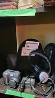 Bose QuietComfort 3 headphones with carrying case, Nikon Coolpix 895 camera, and cables on shelf.
