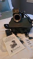 Photo of Pentax camera with attached Sigma lens and PhotoMed TTL Ring/Point flash system on top of green Sigma camera bag along with instruction manual and battery charger visible nearby.