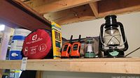Shelving with camping items including Outbound sleeping bag in red bag, two orange and black Motorola walkie talkies, a green and silver camping lantern with handle, and blue and white water cooler.