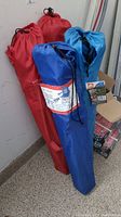 Four camping chairs in closed carrying bags, two red, one blue prominently shown with label.