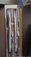 Two two-toned Cross pen and pencil sets inside original clear plastic packaging, silver with gold trim accents.