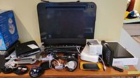 Multiple electronic items on table including earphones, smart watches, charging cables, and small devices.