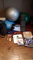 Photo of exercise balls, two mats, scales, resistance tubing box, P90X DVD, shoe stretcher, and fitness accessories on floor.
