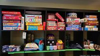 Shelves containing multiple boxed board games in a variety of classic titles, foam dice, poker chip set, and other game accessories.