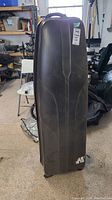 Front view of black hard shell golf travel case standing upright showing scuffed surface and seller tag.